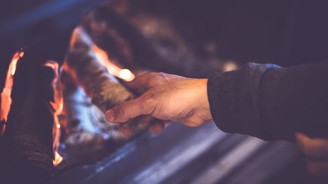 Mies kohentaa takkatulta.