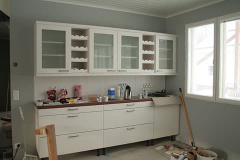 <p data-block-key="h45ef">Keittiön päätyseinä, jonka eteen tulee pirttiryhmä. Olohuone avautuu vasemmalle. Puustellin vaaleassa kaapistossa on wanhanajan tunnelmaa.</p>