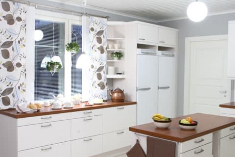 <p data-block-key="dx7bi">Tasojen punertava puuväri lämmittää vaalean Puustellin keittiön. Keittiössä jatkuu olohuoneen verhojen lehtikuosi yhdistettynä valkoiseen. Ruskeat keittiöpyyhe ja patalappu täydentävät kokonaisuutta.</p>