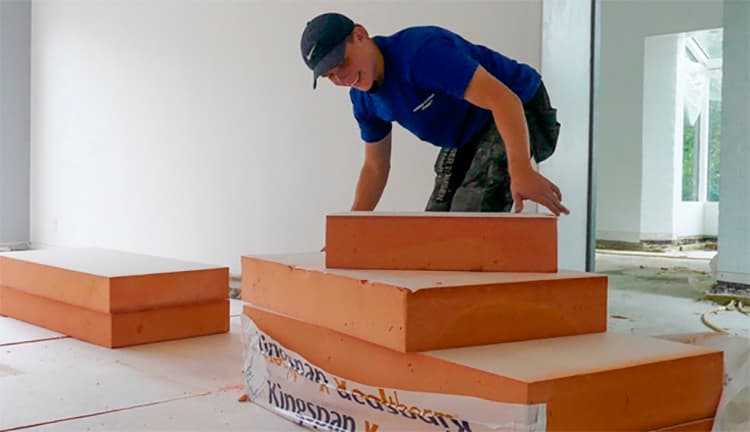 Hymyilevä sinipaitainen asentaja asentaa Kingspan-eristeitä paikoilleen.