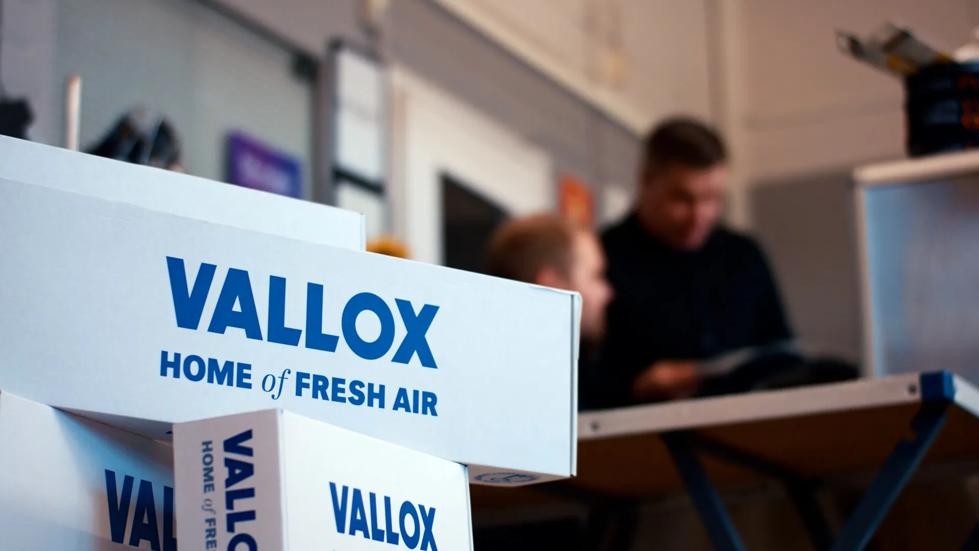 Ihmiset pöydän ääressä tutkimassa papereita ja vierellä Vallox ilmanvaihtosuodattimia