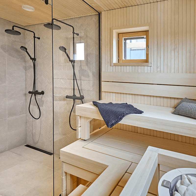 Kastellin hirsi ja pesäpuu rakennuksen suihkutilat ovat valoisat, ikkunalliset ja materiaalivalintoina on saunassa vaalea puu ja suihkutiloissa harmaa laatta.