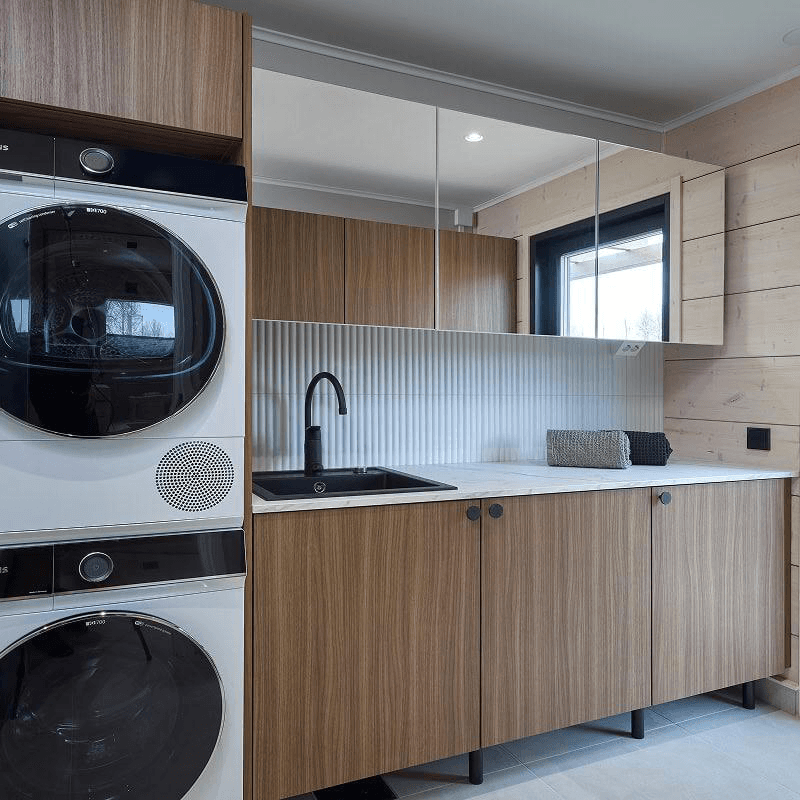 Kastellin kodinhoitohuone näyttäytyy käytännölliseksi suuren pöytätilan ansiosta. Peiliovet luo tilantuntua ja tummat kaapit luovat hienon kontrastin vaaleaa hirsitalon runkoa vasten.