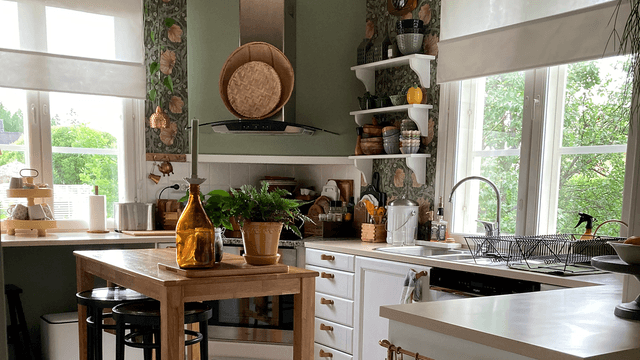 Värikäs ja kodikas keittiö, jossa vaaleanvihreät seinät, William Morrisin Pimpernel-tapetti ja valkoiset kaapistot. Tammiset avohyllyt, puinen saarekepöytä ja viherkasvit tuovat tilaan lämpöä. Suuret ikkunat päästävät runsaasti luonnonvaloa sisään.