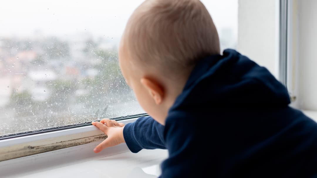lapsi koskettaa sisäpuolelta märkää ikkunaa huoneessa, jossa sisäilma kosteus on korkea