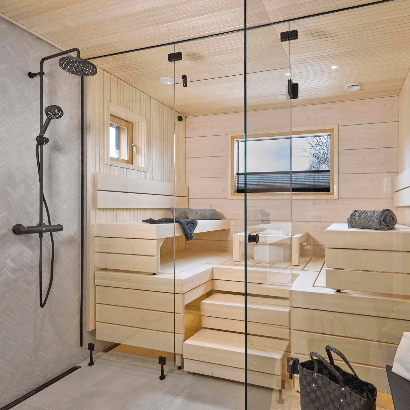 Kastellin hirsi ja pesäpuu rakennuksen suihkutilat ovat valoisat, ikkunalliset ja materiaalivalintoina on saunassa vaalea puu ja suihkutiloissa harmaa laatta.