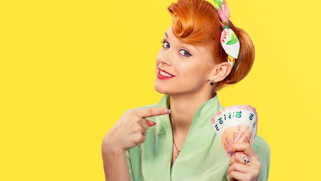 punatukkainen nainen vaaleanvihreässä asussa osoittaa kummenen euron rahatukkua kädessään