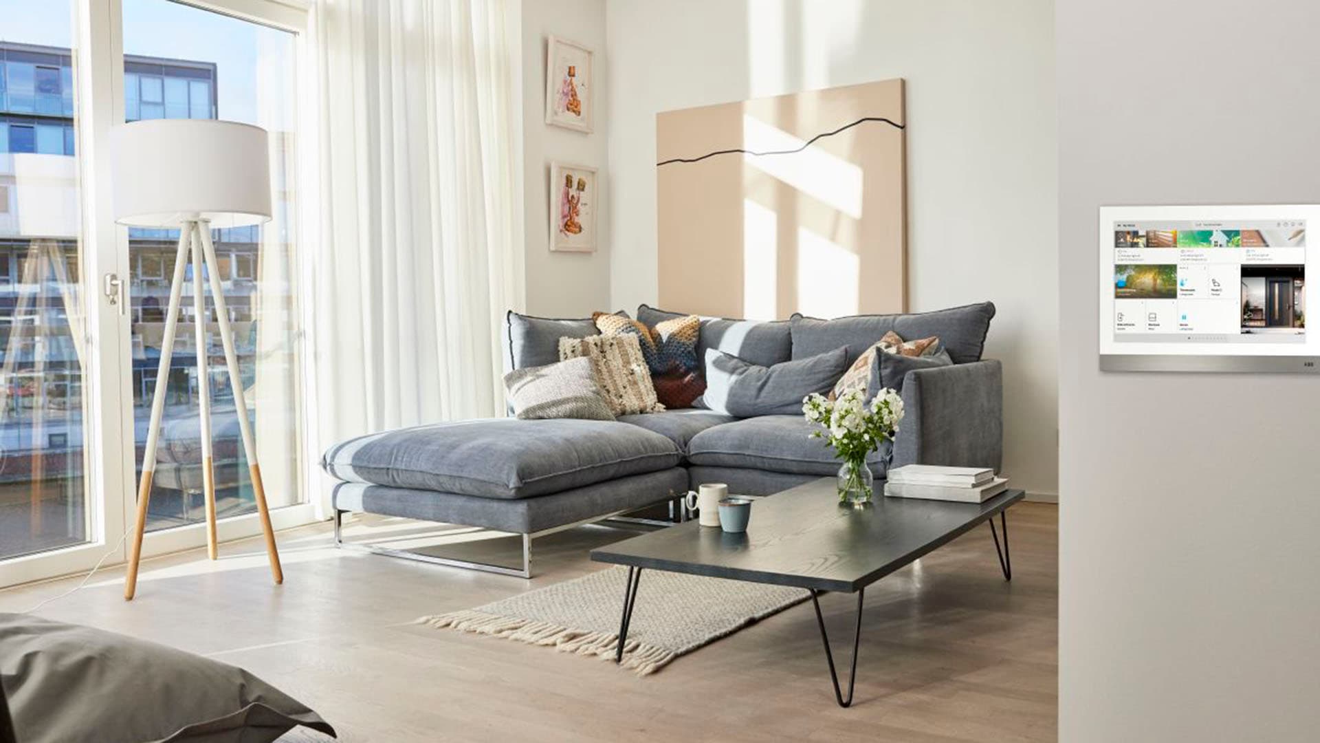 Olohuone jossa harmaa sohva seinällä näkyy ABBn free@home kodinohjausjärjestelmä