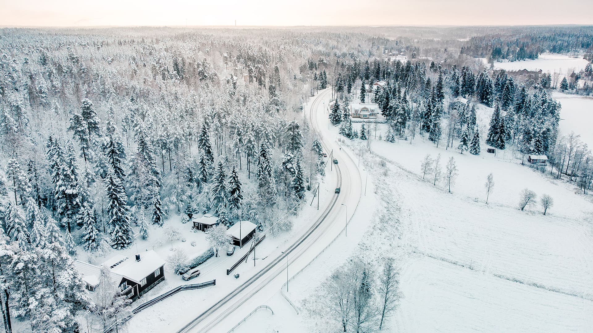 Talvinen ilmakuva maisemasta, jossa näkyy muutamia taloja, maantie sekä metsää.
