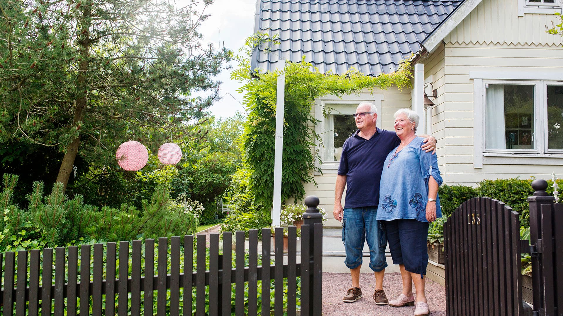Iloinen vanhempi pariskunta seisoo omalla tontillaan