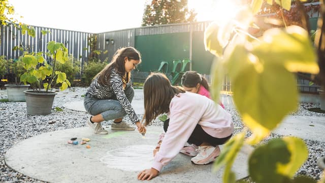 Kolme lasta piirtämässä iloisia kuvia pihakiveykselle