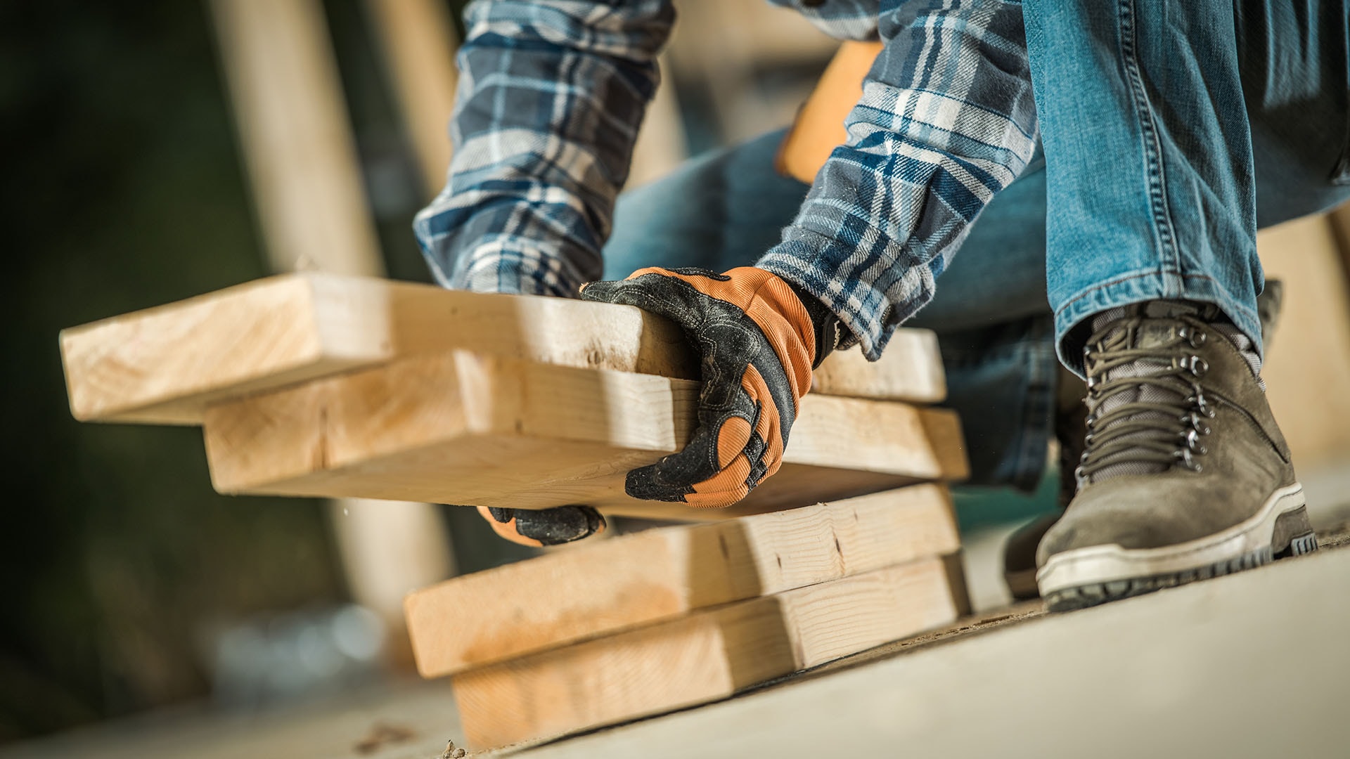 mies nostaa puutavaraa lattialta kädessään oranssi-mustat työhanskat