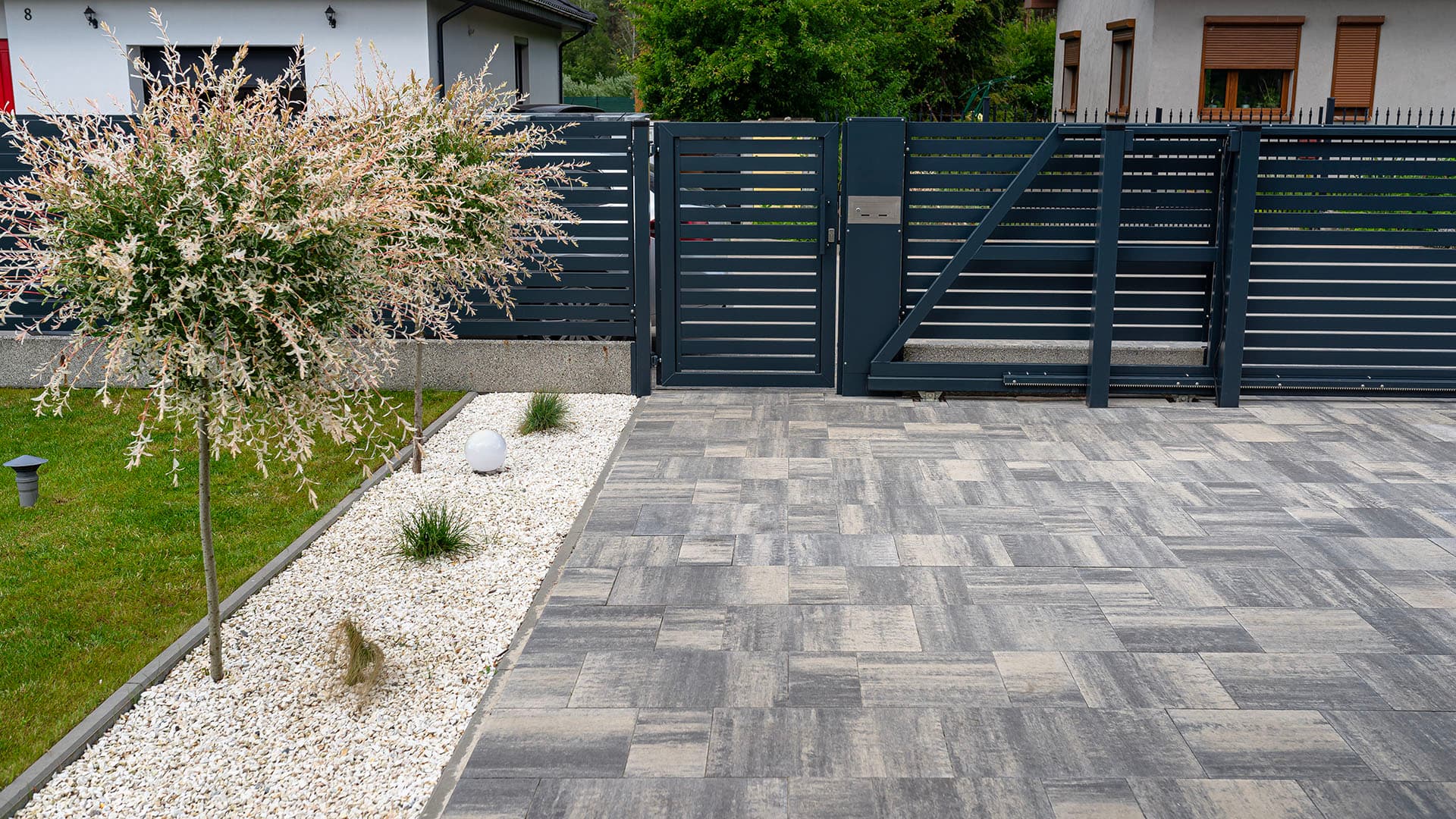 Laajempi kivetty piha-alue, joka rajautuu kadun suuntaan mustaan aitaan.