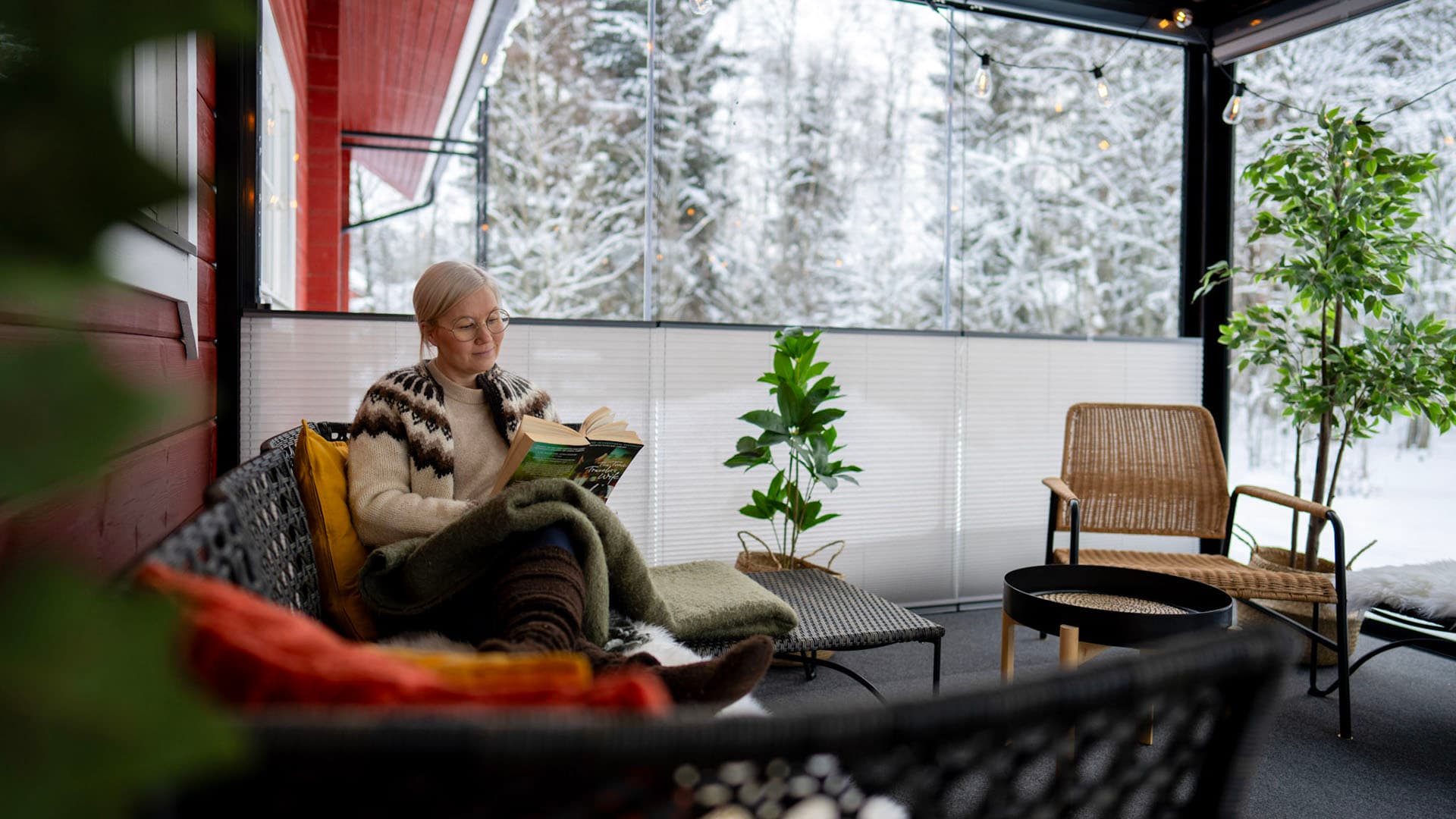 nainen istuu lukemassa lasitetulla terassilla