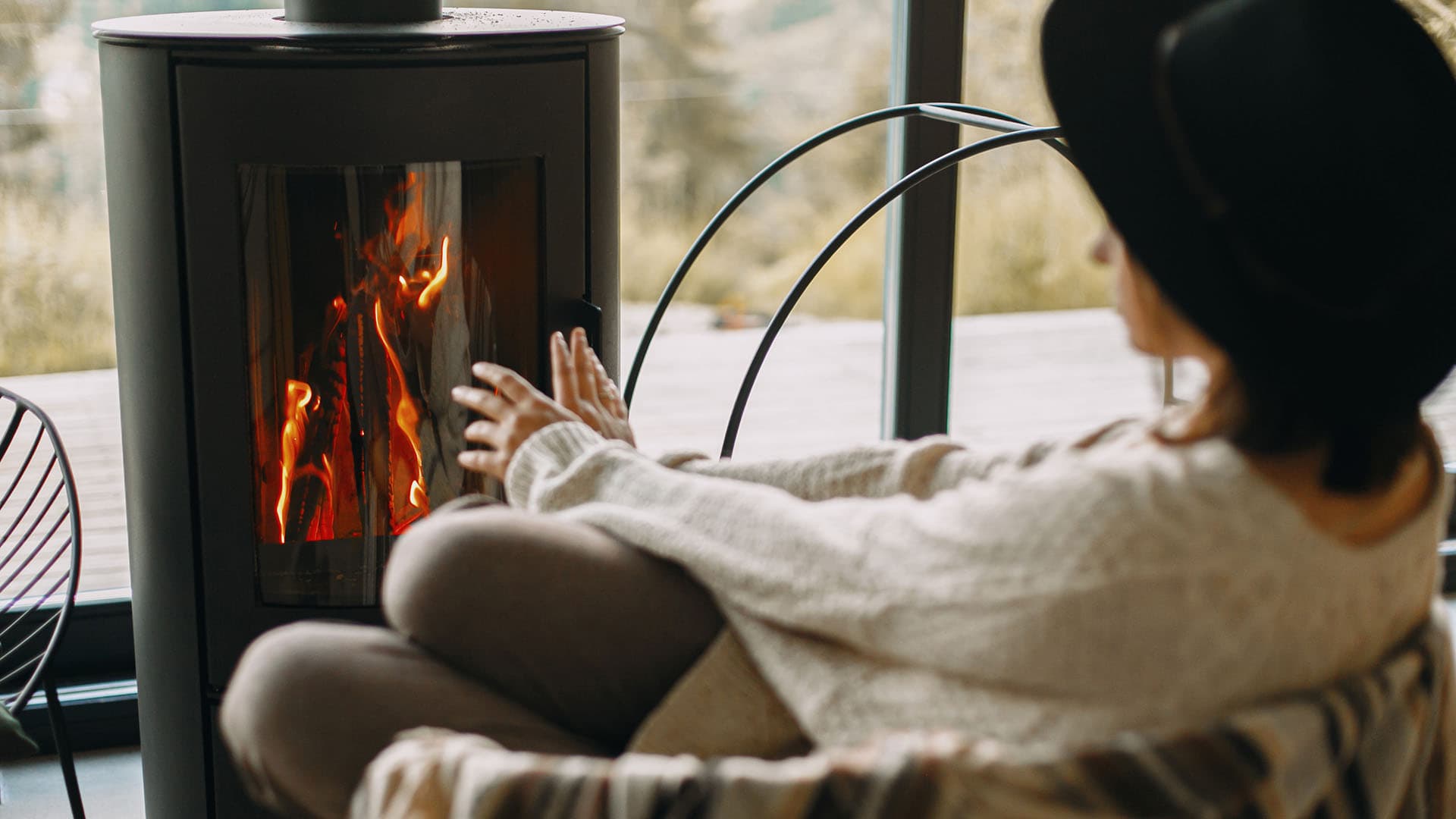 nainen lämmittelee käsiään mustan kamiinan edessä