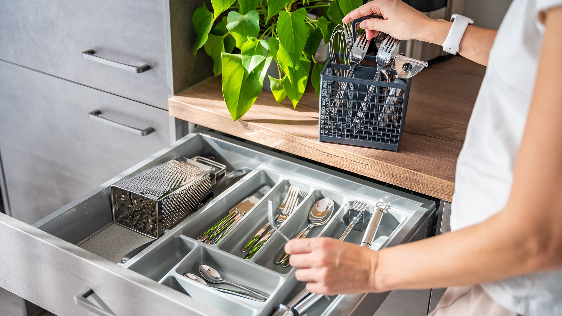 nainen siirtää ruokailuvälineitä tiskikoneen pesukorista laatikkoon