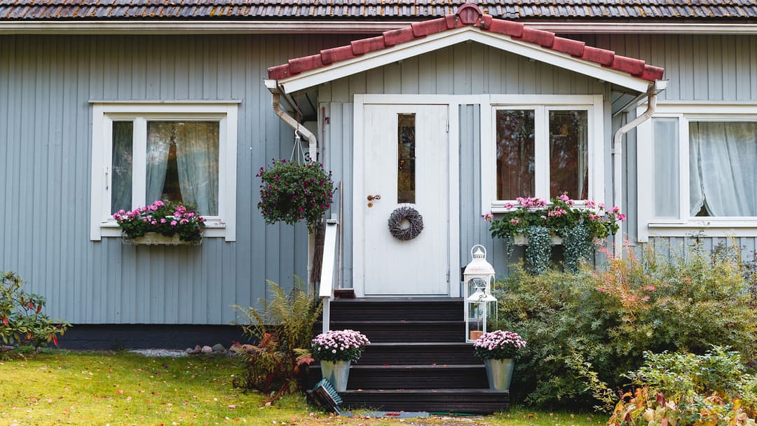 Puinen vanha vaaleansininen omakotitalo, jonka kuistin vierellä kasvaa istutuksia