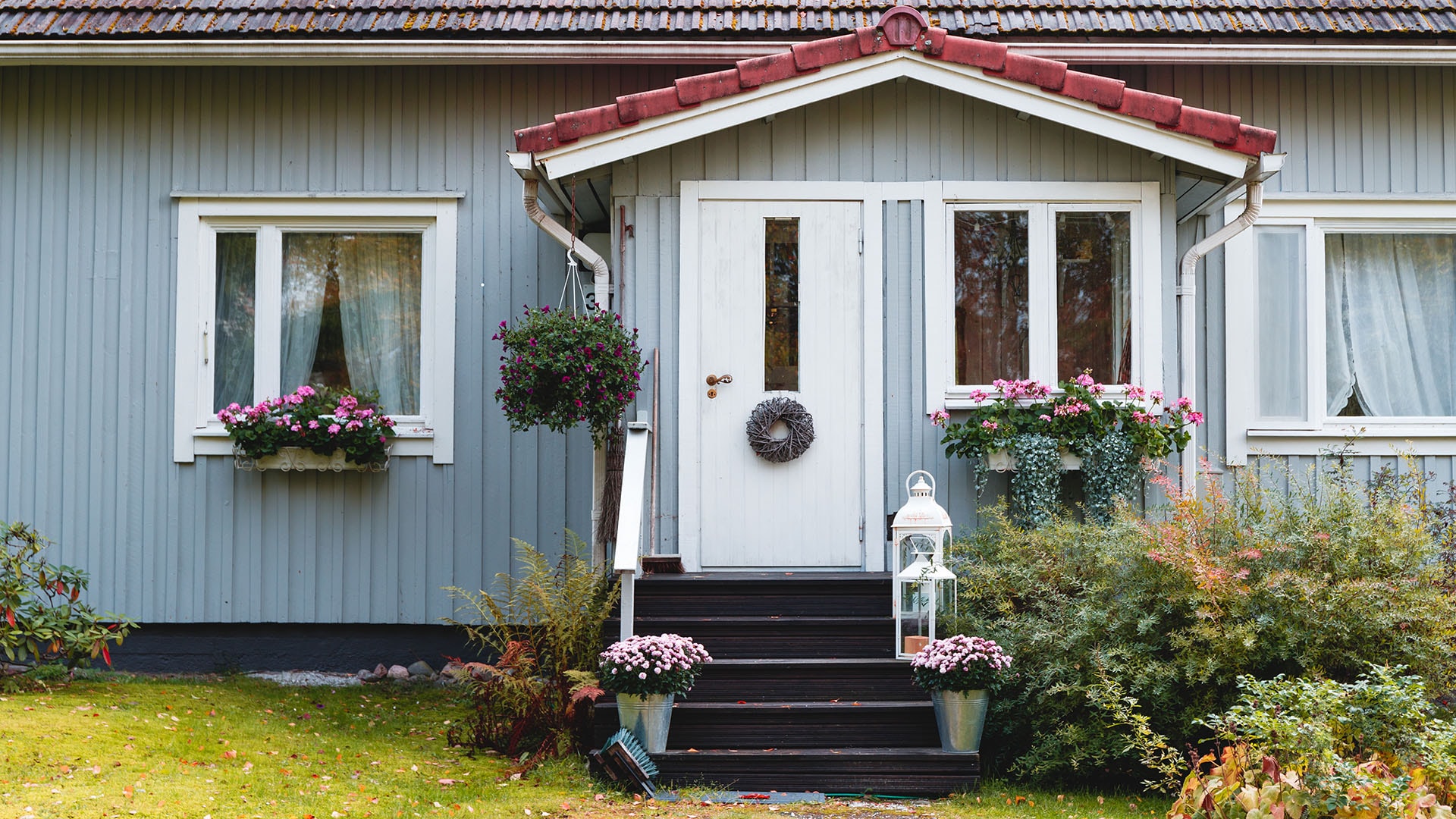 1920 puinen vaaleansininen omakotitalo jonka kuistin vierellä kasvaa istutuksia