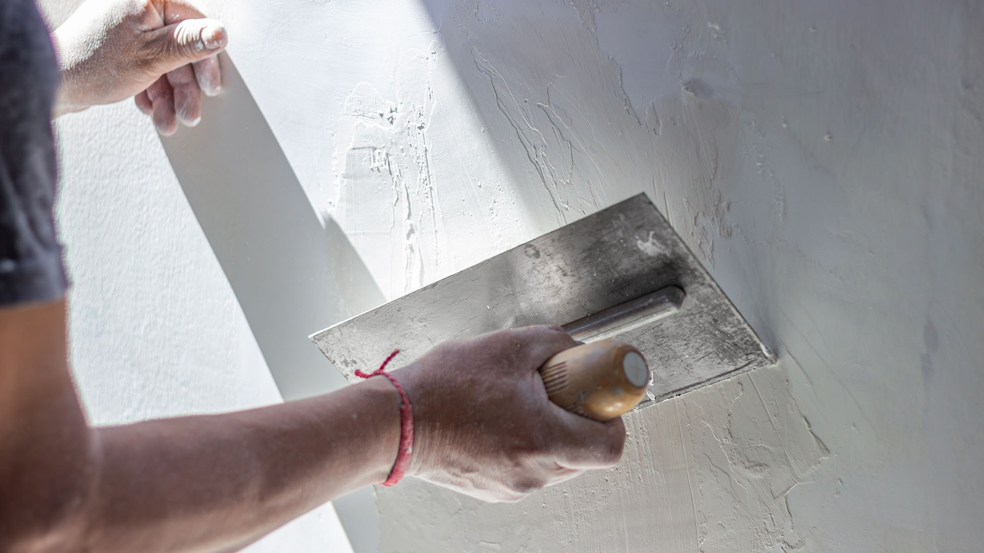 1920 rakennusmies laittaa vaaleaa tasoitetta seinään lastan avulla