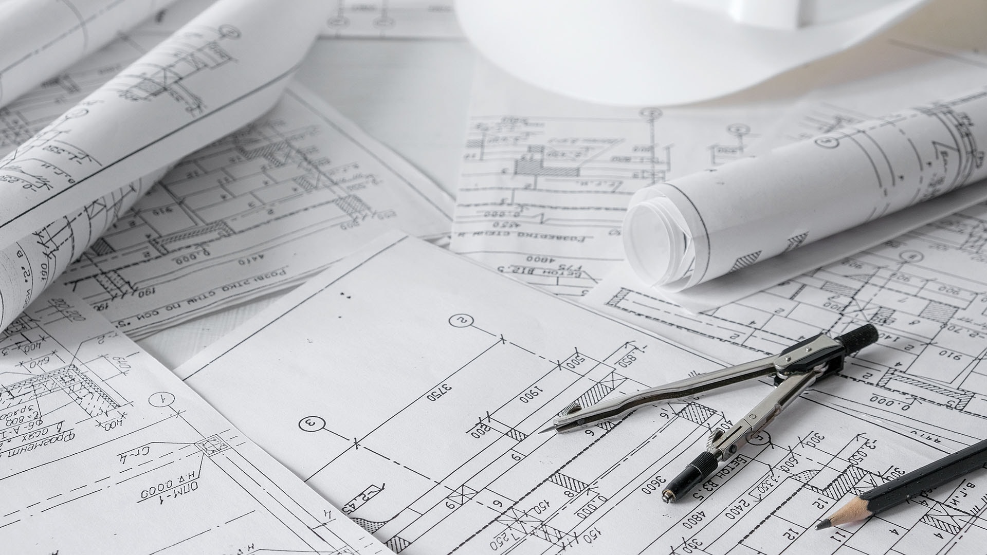 1920 rakennuspiirustuksia ja leikkauskuvia pöydällä paperien päällä kynä harppi ja kypärä