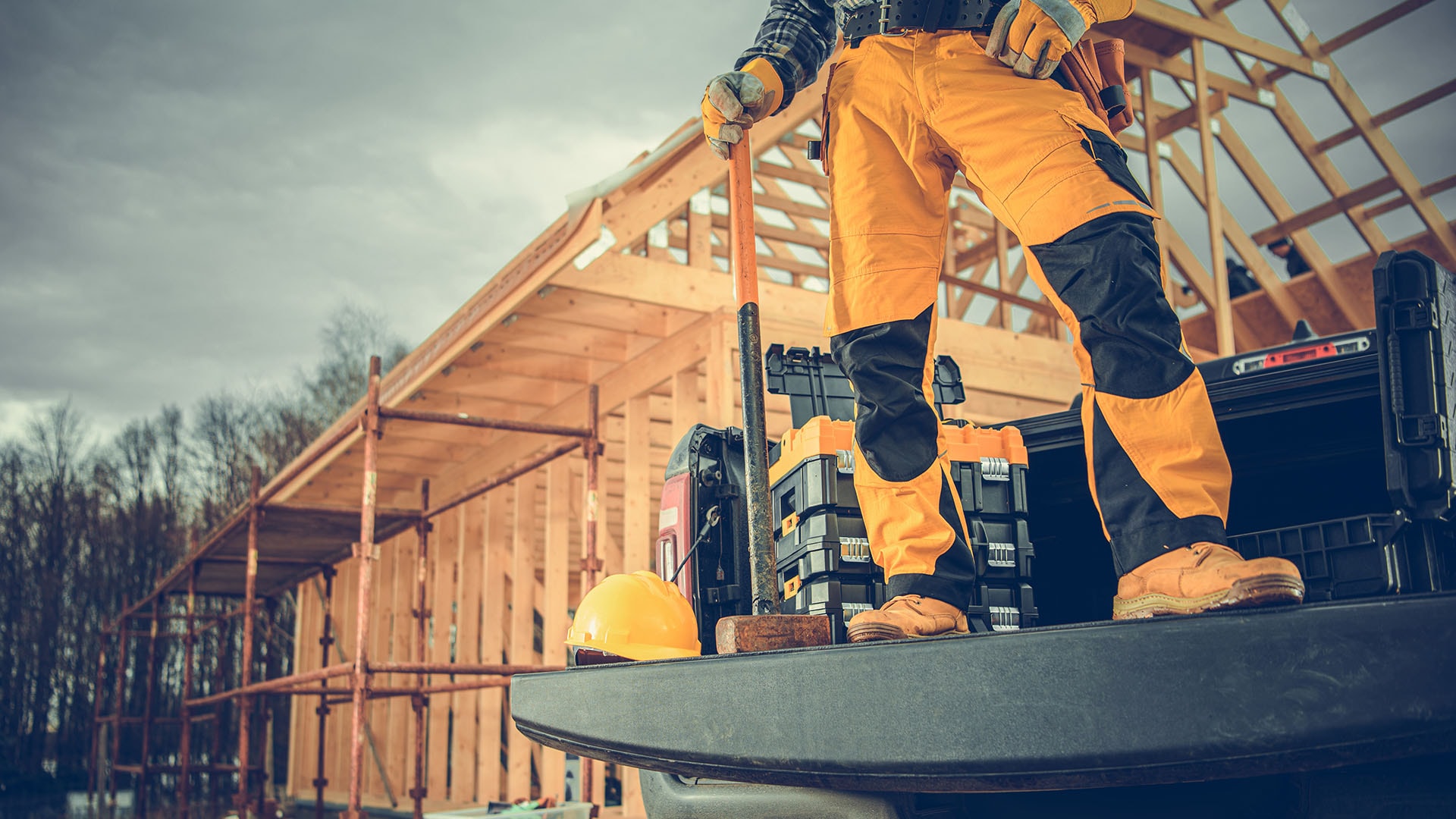 1920 rakennustyömies seisoo avolava-autonsa lavalla kädessään leka taustalla rakennustyömaa