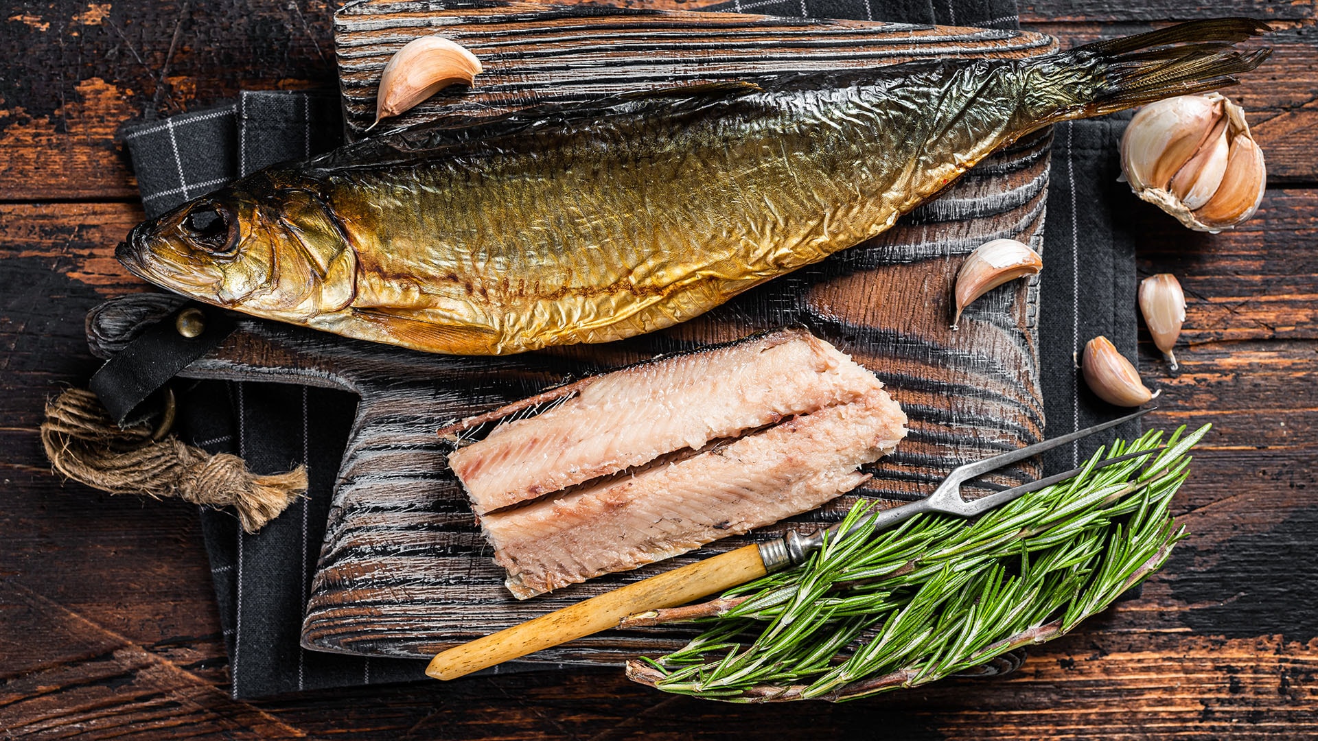 1920 savustettu kala puutarjottimella ympärillä valkosipulia ja yrttejä