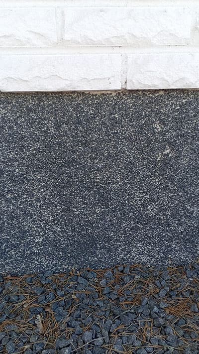 musta rouhepinnoitus vaalealla pohjalla yläpuolella valkoista tiiliseinää MR