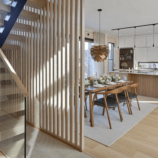 Hirsi-Kastelli Pesäpuu Oulu 1 on asunto joka oli asuntomessuilla 2025 Puinen portaikko ja keittiöratkaisu. Värimaailmassa lattia ja portaikko on vaaleaa puuta ja kalusteet tummaa puuta ja seinät ovat valkoisia.