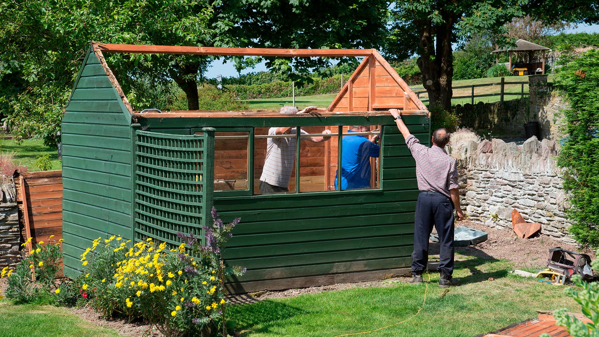 kolme henkilöä rakentaa mökkiä pihalla