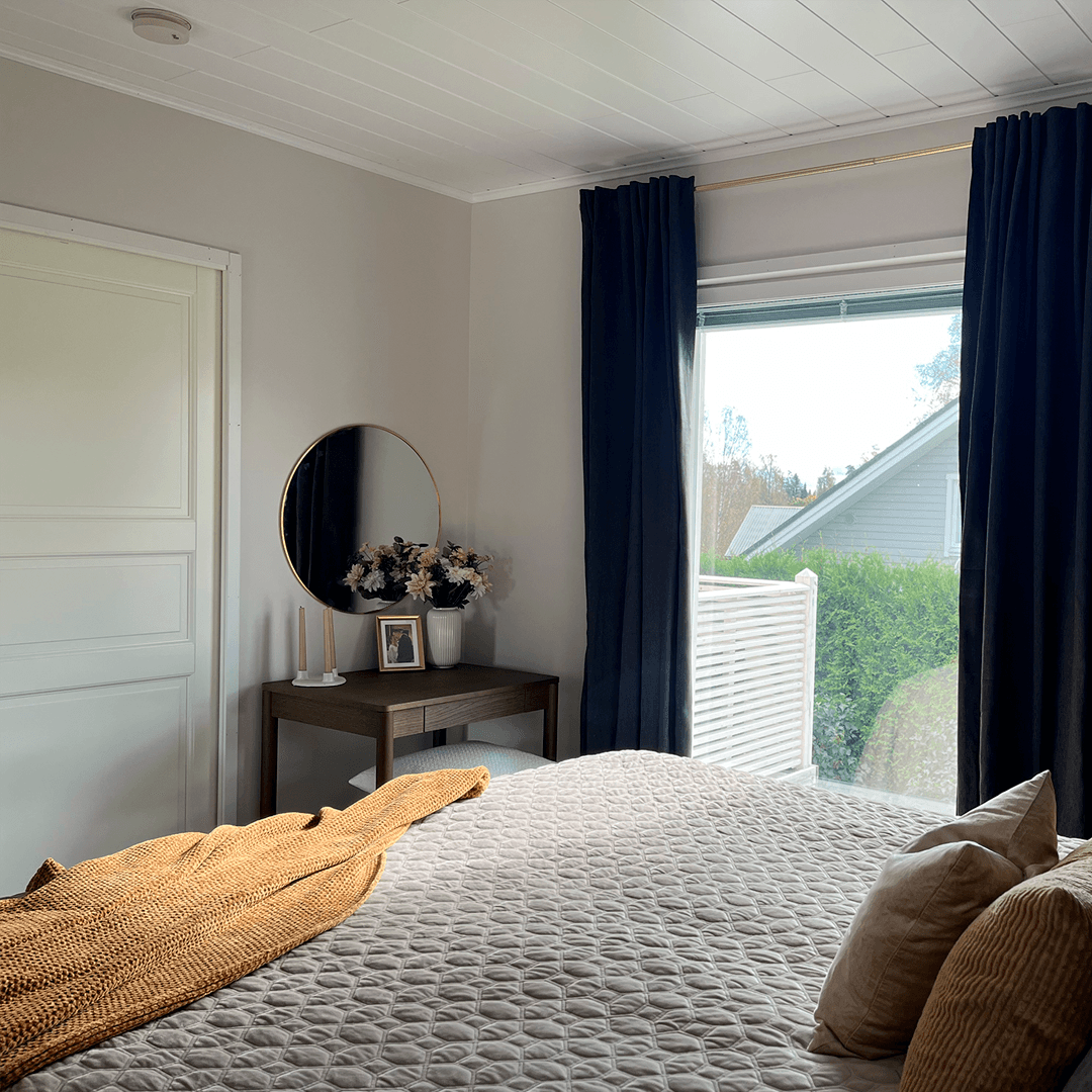 makuuhuoneen ikkunasta näkyy maisema ja sisällä on tummat verhot